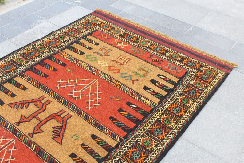 May include: A traditional rug with a geometric pattern in shades of red, brown, black, and green. The rug has a fringe border and is made of wool.