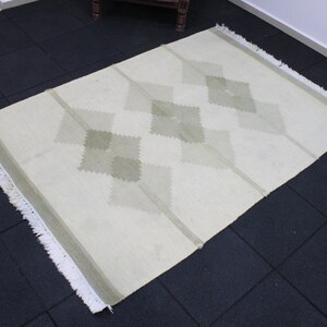 May include: A white rug with a diamond pattern in a light green color. The rug has a fringe border.