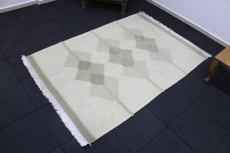 May include: A white rug with a diamond pattern in a light green color. The rug has a fringe border.