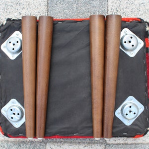 May include: Four wooden legs with metal plates attached to the bottom of a red, black, and white patterned ottoman.