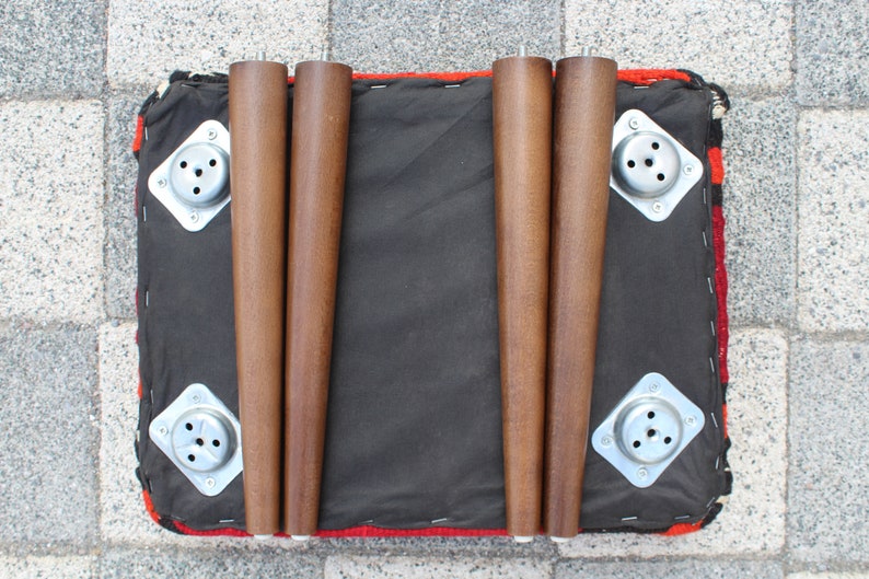 May include: Four wooden legs with metal plates attached to the bottom of a red, black, and white patterned ottoman.