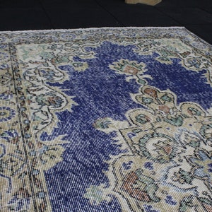 May include: A vintage rug with a blue center and a cream-colored border. The rug has a floral pattern with intricate details.