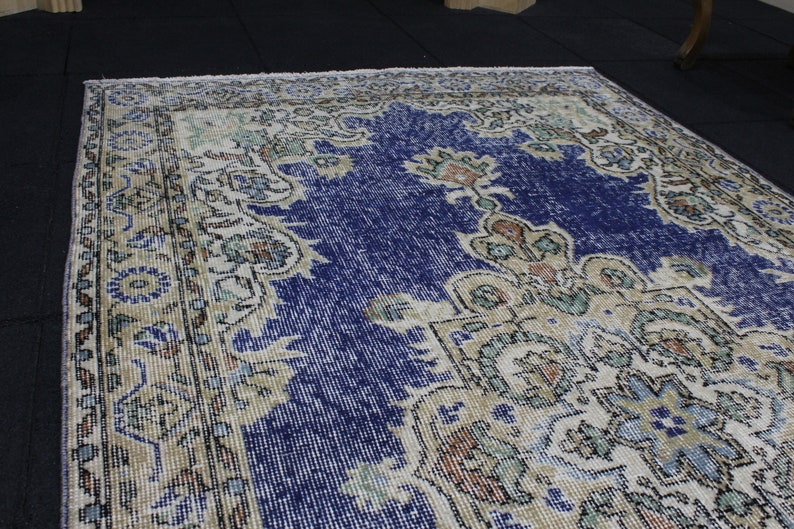 May include: A vintage rug with a blue center and a cream-colored border. The rug has a floral pattern with intricate details.