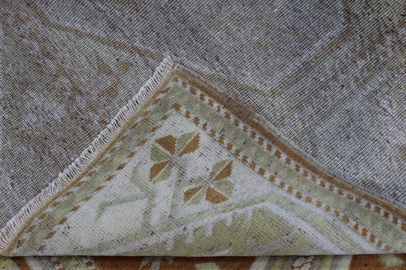 May include: Close-up of the back of a rug with a light brown and white geometric pattern. The rug has a fringe border.