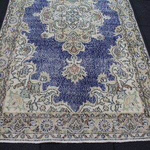 May include: A vintage rug with a blue and cream color scheme. The rug has a floral pattern with a central medallion. The rug is worn and faded, giving it a distressed look.