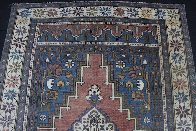 May include: A traditional rug with a blue and red center surrounded by a border of white, green, and brown geometric patterns.