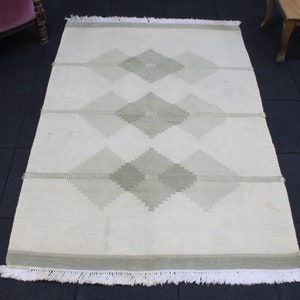 May include: A white rug with a geometric pattern of light green diamonds. The rug has a fringe border.