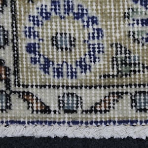 May include: Close-up of a beige rug with a blue and white floral pattern. The rug has a fringe border.