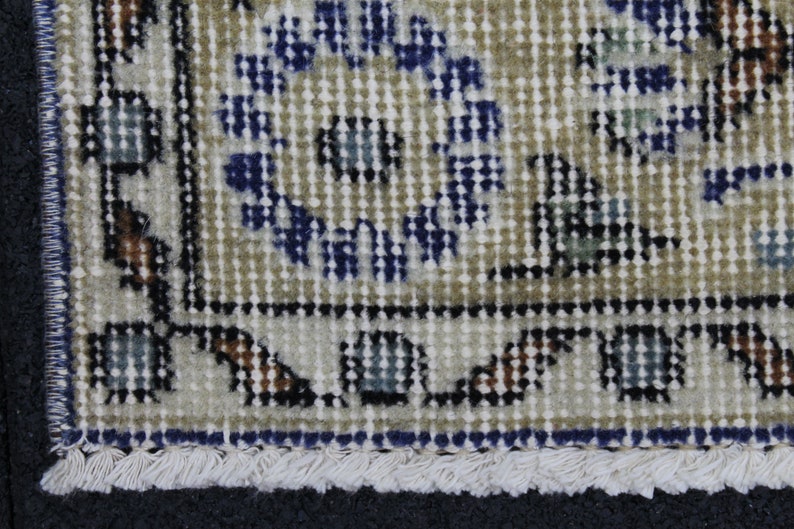 May include: Close-up of a beige rug with a blue and white floral pattern. The rug has a fringe border.