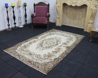 May include: A cream-colored rug with a brown floral pattern. The rug is laid out on a black tiled floor.