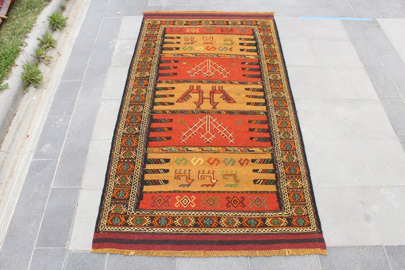 May include: A traditional Turkish rug with a red, orange, and black geometric pattern. The rug has a fringe border and is made of wool.