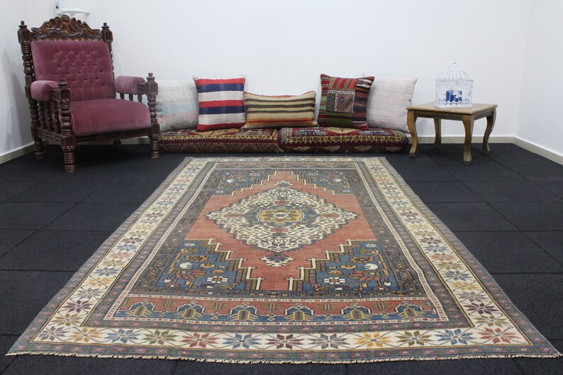 May include: A vintage rug with a traditional Persian design. The rug has a red center with a blue and white geometric pattern. The rug is surrounded by a cream-colored border with a floral design.