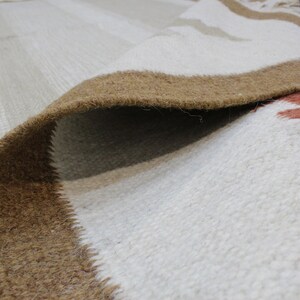 Puede incluir: Primer plano de una alfombra tejida blanca y marr&oacute;n con una superficie texturizada. La alfombra tiene un borde marr&oacute;n y un centro blanco con un patr&oacute;n sutil.