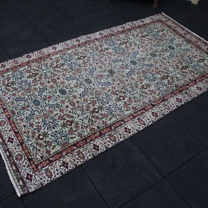May include: A cream-colored rug with a floral pattern in shades of red, blue, and green. The rug has a border with a repeating pattern of red, white, and blue.