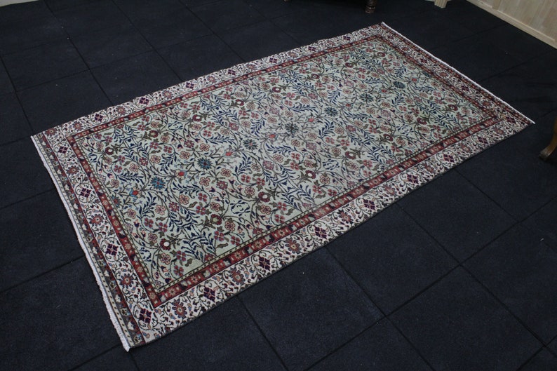 May include: A cream-colored rug with a floral pattern in shades of red, blue, and green. The rug has a border with a repeating pattern of red, white, and blue.