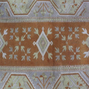 May include: A vintage rug with a brown center and a white and light gray geometric pattern. The rug has a border with a repeating pattern of white and light gray.