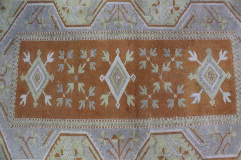 May include: A vintage rug with a brown center and a white and light gray geometric pattern. The rug has a border with a repeating pattern of white and light gray.