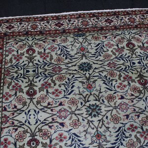 May include: A cream-colored rug with a floral pattern in shades of pink, blue, and brown. The rug has a border with a red and white pattern.