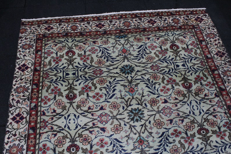 May include: A cream-colored rug with a floral pattern in shades of pink, blue, and brown. The rug has a border with a red and white pattern.