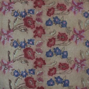 May include: A beige floral rug with a repeating pattern of red, pink, and blue flowers. The rug has a distressed look, with faded colors and a worn texture. The flowers are stylized and arranged in a symmetrical design.
