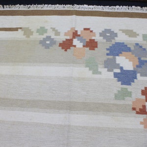 Puede incluir: Una alfombra blanca con un borde marr&oacute;n y un dise&ntilde;o floral en tonos de azul, verde, rojo y rosa.