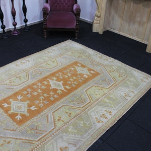 May include: A vintage rug with a light orange center and a white and light yellow border. The rug has a geometric pattern with diamond shapes and floral motifs.