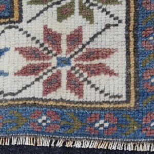 May include: Close-up of a woven rug with a white background and a colorful floral pattern. The rug has a blue, red, and green border.