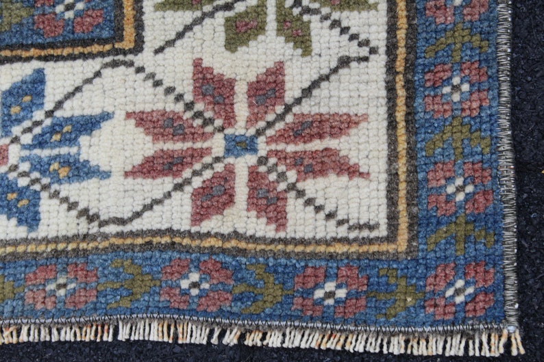 May include: Close-up of a woven rug with a white background and a colorful floral pattern. The rug has a blue, red, and green border.