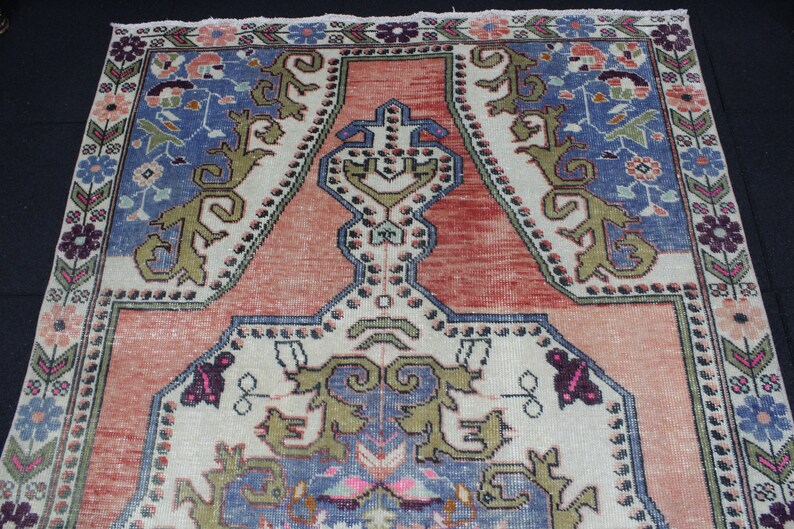 May include: A vintage Turkish rug with a traditional design. The rug has a cream background with a red center and blue and green accents. The rug is decorated with floral and geometric patterns.