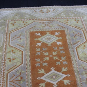 May include: A vintage rug with a geometric pattern in shades of beige, brown, and white. The rug has a central diamond shape with a smaller diamond inside. The rug is surrounded by a border of smaller geometric shapes.