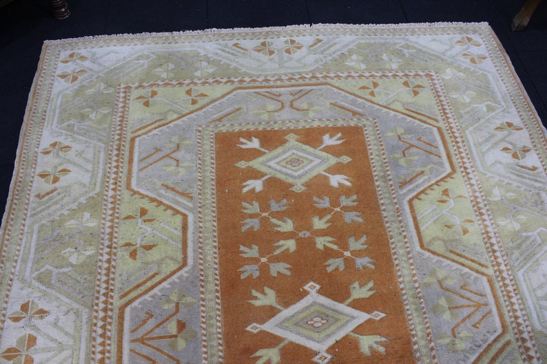 May include: A vintage rug with a geometric pattern in shades of beige, brown, and white. The rug has a central diamond shape with a smaller diamond inside. The rug is surrounded by a border of smaller geometric shapes.