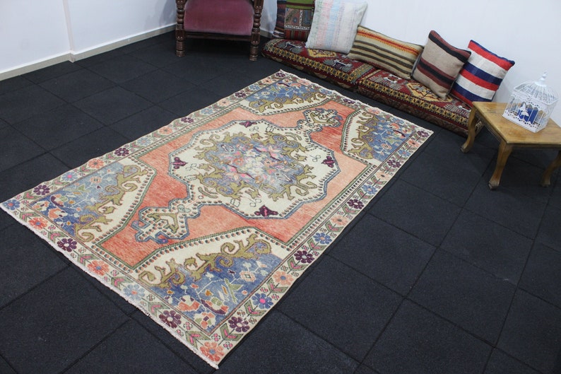May include: A vintage Turkish rug with a cream background and a central medallion in shades of peach, blue, and green. The rug has a floral border with a repeating pattern of flowers and leaves.