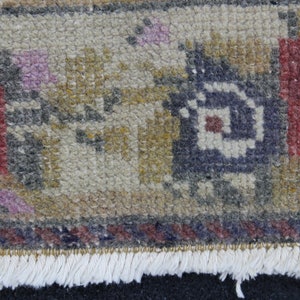 May include: Close-up of a section of a small, hand-woven rug. The rug features a complex pattern with colors including red, blue, yellow, and purple. The rug has a fringe along one edge.