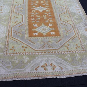 May include: A vintage Turkish rug with a geometric pattern in shades of beige, brown, and orange. The rug has a fringe border.