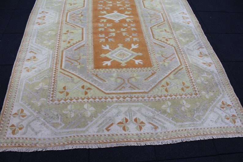 May include: A vintage Turkish rug with a geometric pattern in shades of beige, brown, and orange. The rug has a fringe border.