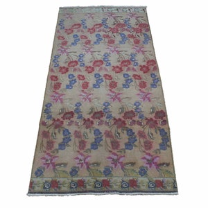 May include: Rectangular beige rug with a floral pattern in red, blue, and pink. The rug features rows of stylized flowers and foliage, with a border of similar design. The rug is suitable for a living room or bedroom.