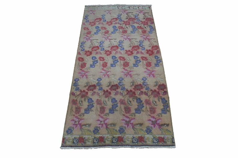 May include: Rectangular beige rug with a floral pattern in red, blue, and pink. The rug features rows of stylized flowers and foliage, with a border of similar design. The rug is suitable for a living room or bedroom.
