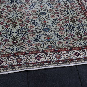 May include: A vintage rug with a cream background and a floral pattern in shades of red, blue, and green. The rug has a border with a repeating pattern of flowers and leaves.