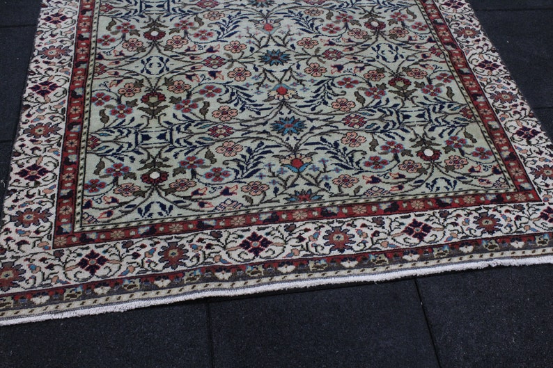 May include: A vintage rug with a cream background and a floral pattern in shades of red, blue, and green. The rug has a border with a repeating pattern of flowers and leaves.