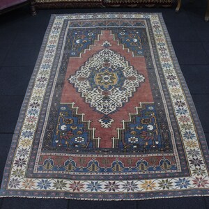 May include: A vintage rug with a red, blue, and white geometric pattern. The rug has a floral border and a central medallion.
