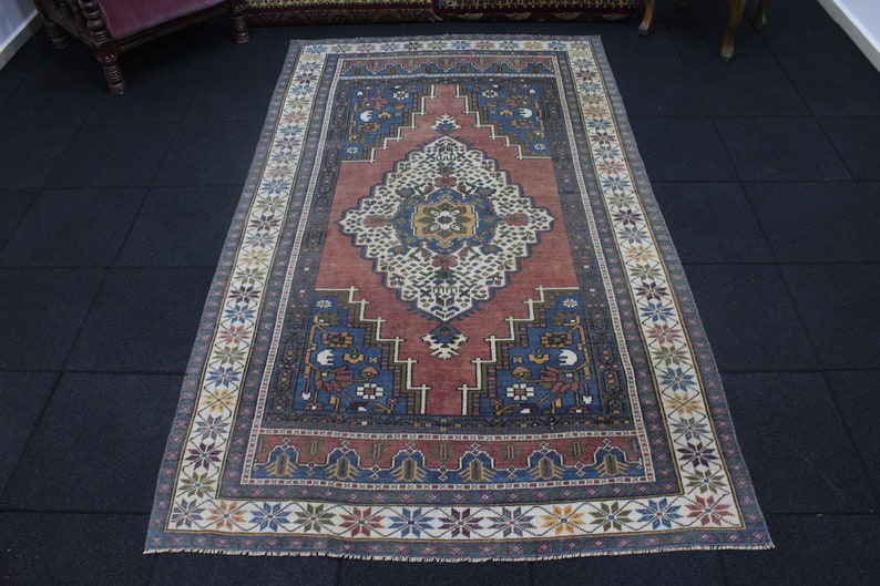 May include: A vintage rug with a red, blue, and white geometric pattern. The rug has a floral border and a central medallion.