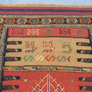 May include: A traditional rug with a red, brown, and black background. The rug has a geometric pattern with intricate details in shades of green, yellow, and blue.