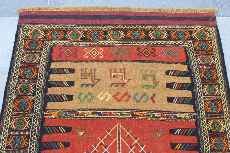 May include: A traditional rug with a red, brown, and black background. The rug has a geometric pattern with intricate details in shades of green, yellow, and blue.