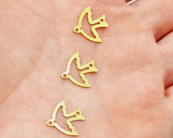 May include: Three gold-colored metal bird charms in the shape of a dove. The charms are on a hand.