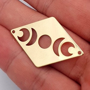 May include: Two gold-colored metal charms in the shape of a diamond with a moon phase design cut out.