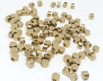 May include: A large group of gold-colored metal beads with a hole in the center of each bead. The beads are scattered on a white surface.