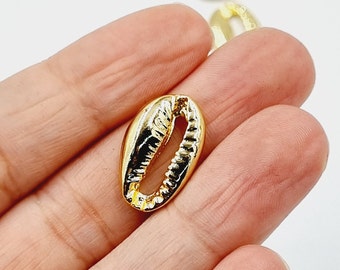 May include: Close-up of several gold-colored cowrie shell charms. The charms are oval-shaped with a slit opening and a glossy finish. The shells are a popular choice for jewelry making and other craft projects.