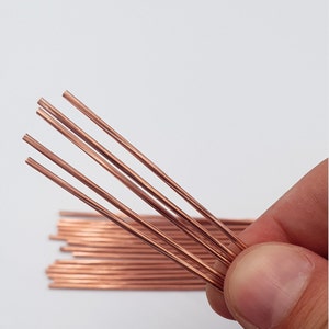 Könnte beinhalten: Ein Bündel dünner, kupferfarbener Metallstäbe. Die Stäbe sind fächerförmig angeordnet und werden in einer Hand gehalten.