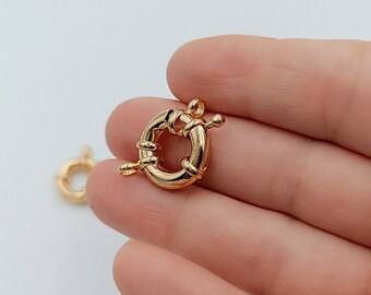 Könnte beinhalten: Goldfarbener Metallverschluss mit rundem, gedrehtem Design. Der Verschluss ist offen und bereit, an eine Halskette oder ein Armband befestigt zu werden.