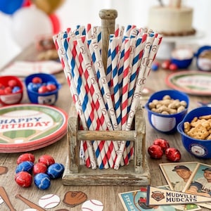 May include: A bundle of paper drinking straws featuring red and blue diagonal stripes and small baseball illustrations, held upright in a weathered wooden stand with a central post. The straws are arranged in a dense, vertical cluster.